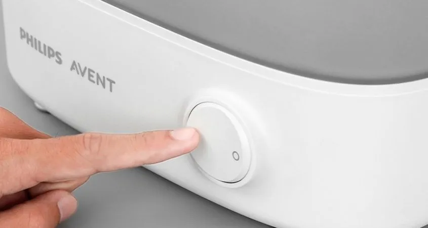 Bật công tắc để khởi động máy tiệt trùng bình sữa sau khi đã đậy kín nắp, đảm bảo quá trình hoạt động diễn ra an toàn và hiệu quả