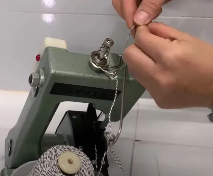 Hướng dẫn bước 2 xỏ chỉ qua lò xo siết chỉ của máy may bao cầm tay.