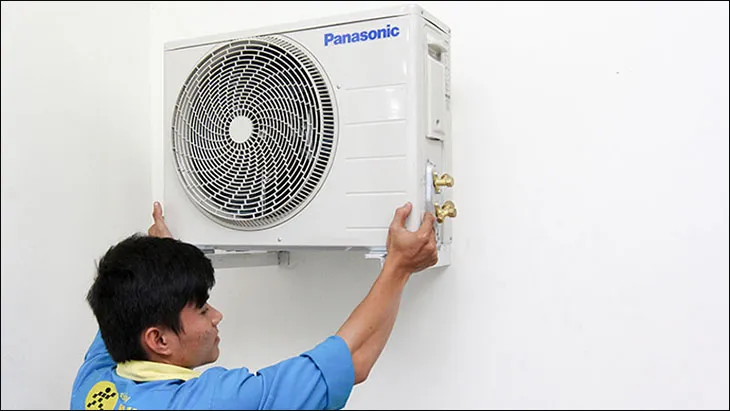Thợ đang thực hiện bước đầu tiên trong cách lắp đặt máy điều hòa: cố định dàn nóng bằng ốc vít trên giá đỡ