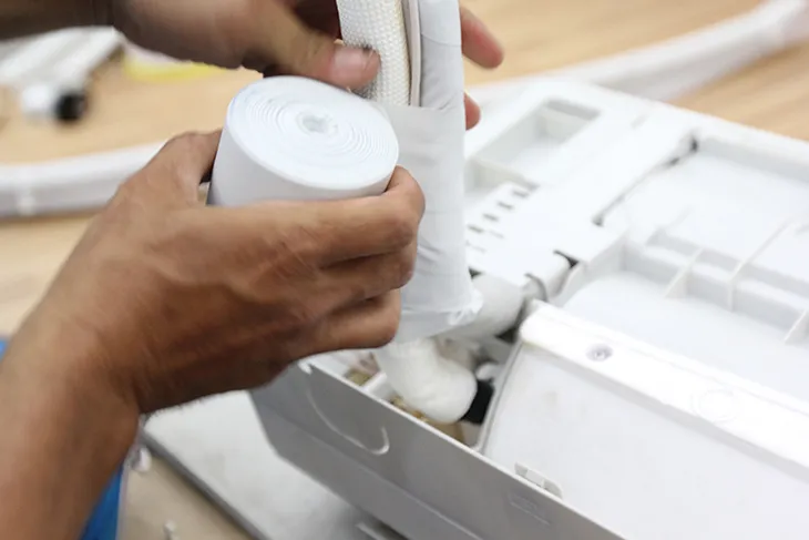 Thợ đang cẩn thận bọc và cuốn băng cách nhiệt cho ống đồng, dây điện và ống thoát nước của điều hòa