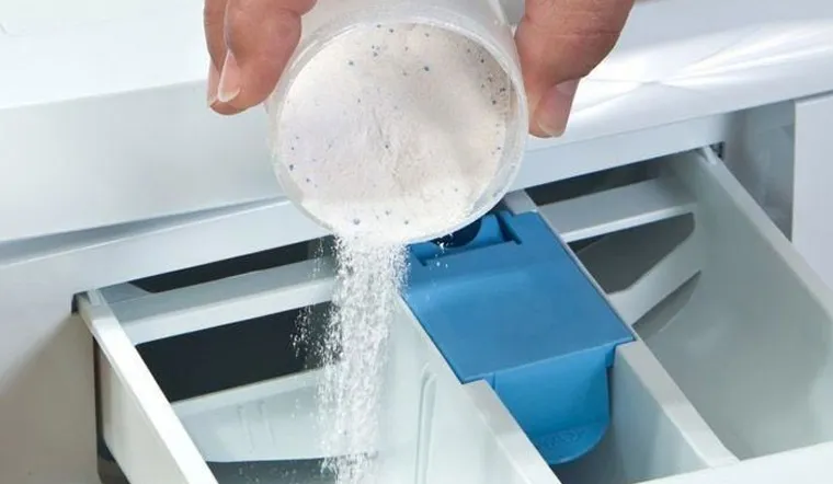 Tay người đang cho nước giặt vào ngăn chứa của máy giặt cửa trên