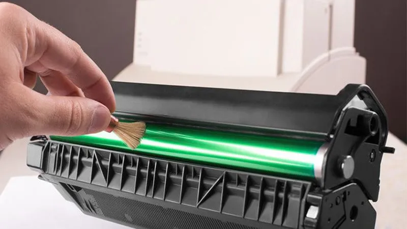 Người dùng đang vệ sinh bên ngoài máy in Canon LBP 2900 bằng khăn ẩm, giữ cho thiết bị sạch sẽ và hoạt động tốt