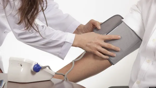 Người đàn ông đang ngồi thoải mái, giữ tay ngang tim để đo huyết áp chính xác