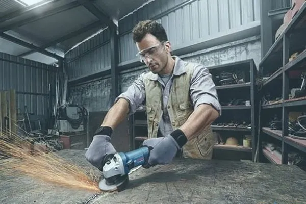 Người thợ trang bị bảo hộ đầy đủ kiểm tra ổ cắm điện trước khi sử dụng máy mài cầm tay để đảm bảo an toàn tối đa.