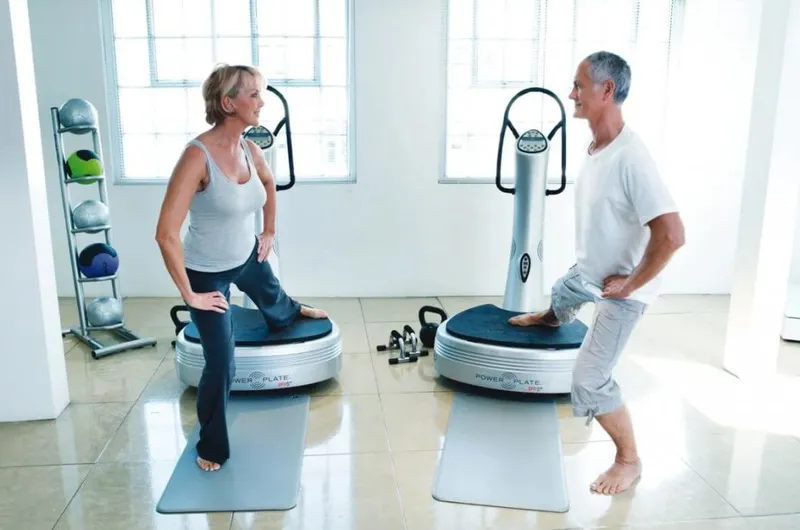 Phụ nữ thực hiện động tác squat trên máy rung toàn thân, minh họa các bài tập và cách sử dụng máy rung toàn thân đa dạng