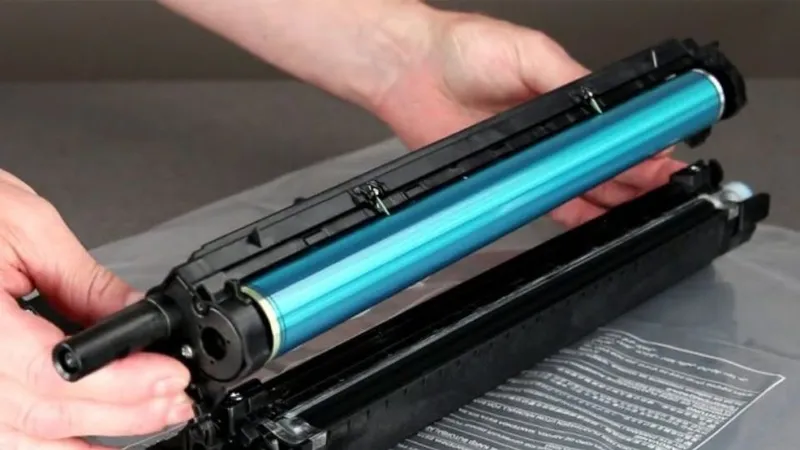 Trống (Drum) trong hộp mực máy in, có hình trụ màu xanh lá cây, đặt trên nền trắng