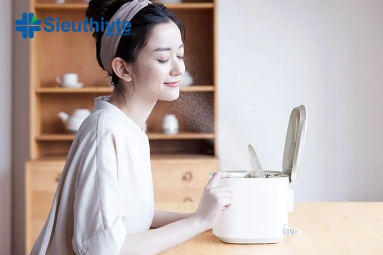 Một người phụ nữ đang xông mặt để làm sạch sâu da bằng máy xông mini